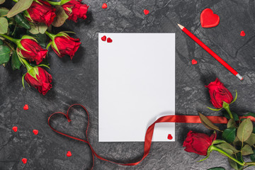 Sheet of paper, pen, hearts, ribbon and red roses on black table. Valentines Day background.