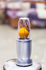 Close view of a blender with an orange and cinnamon sticks on a