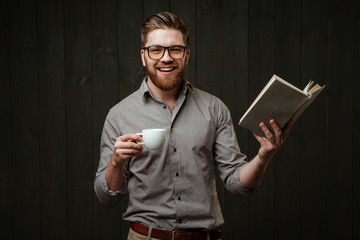 Man in eyeglasses reading book and holding cup of coffee