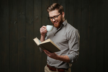 Man in eyeglasses reading book and drinking cup of coffee