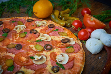 Various ingredients for pizza. Flour, butter, mushrooms, cucumbers, cherry tomatoes, olives,Mozzarella  , sausage, cheese. Dark background.