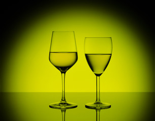 Two wineglasses with white wine on blurred yellow background