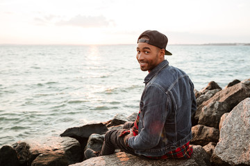 Happy african man wearing cap walking on the beach.