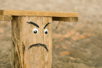 Wooden chair of logs with painted an angry face on the background of sand