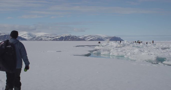 Tourist walks toward group near crack in sea ice with mountains