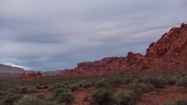 Timelapse of sagebrush and plants with clouds and cliff at sunrise in desert