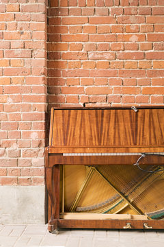 Old abandoned brown piano on a background of red brick wall
