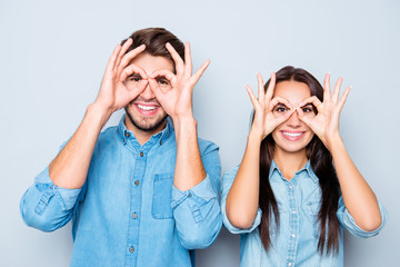 Portrait of two happy funny lovers holding fingers near eyes