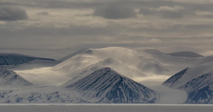 Time lapse - clouds cast shadows over snowy mountains sea ice