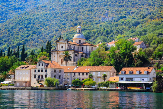 Waterfront of small town Prcanj along Bay of Kotor, Montenegro. View of Birth of Our Lady Church, coastal villas, gardens and mountain from sea.