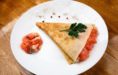 pancake with red fish on a white plate. wooden table.