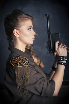 Side portrait of attractive girl holding mauser pistol in hands close to face
