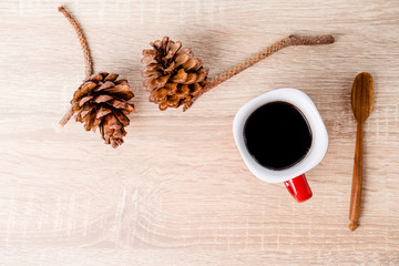 Cup of coffee and brown pine cone on wooden table.