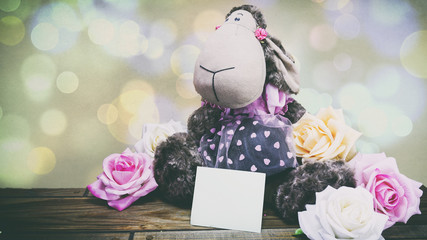 plush lamb and pink roses and a wooden background, a note on the
