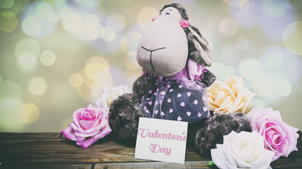 plush lamb and pink roses and a wooden background, a note on the