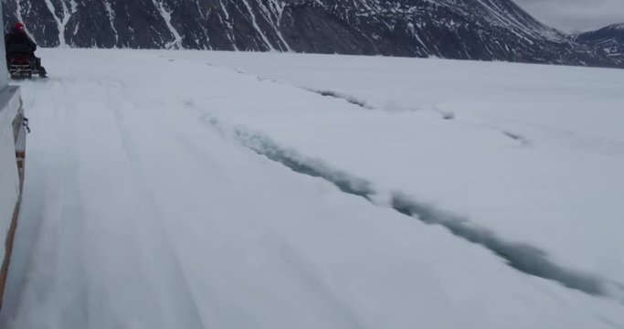 Snow machine pulling trailer next to crack in sea ice