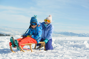 Fototapeta na wymiar Happy children has fun with wooden sled in the mountains on a sunny day