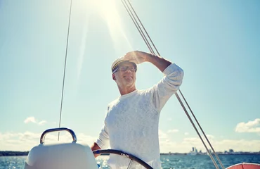 Fototapeten senior man at helm on boat or yacht sailing in sea © Syda Productions