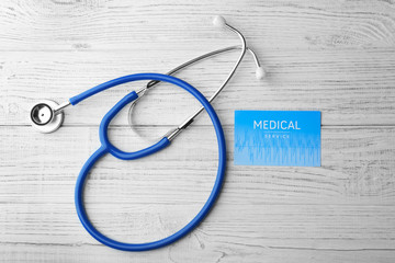 Stethoscope and card on light wooden background