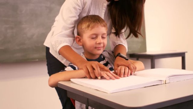 Teacher helping a blind schoolboy with his homework in classroom - Powered by Adobe
