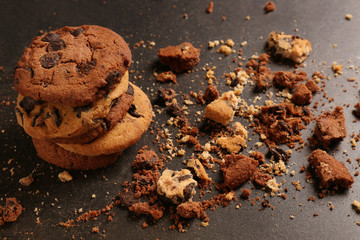 Tasty cookies with chocolate chips and crumbs on dark background