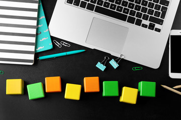 Laptop, copybook and wooden cubes on color background