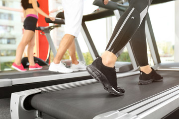 Fototapeta na wymiar Legs of sporty woman running on treadmill in gym, close up view