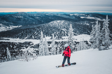 Fototapeta na wymiar Man snowboarder in red jacket goes down from top of snow mountai