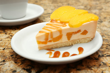 Plate with tasty peach cheesecake on table, close up view