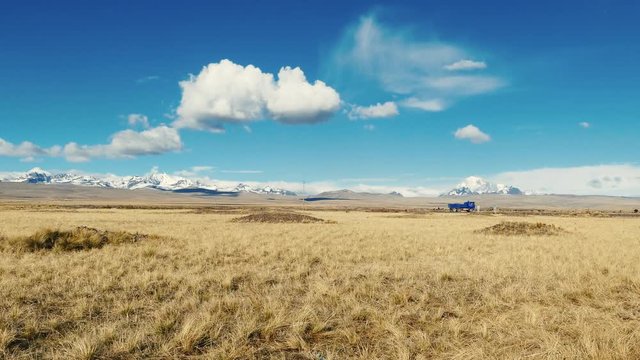 Clip of the Altiplano grassland in Bolivia. A blue truck crosses the scene. The background shows the snowcapped Andes.