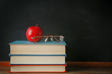Books with glasses and apple on wooden table