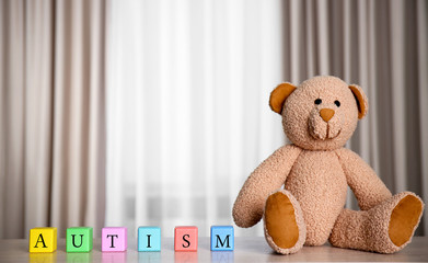 Colorful wooden cubes with Teddy bear on curtains background. Autism concept