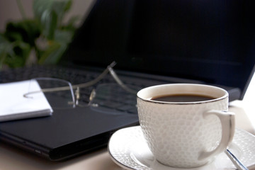 Blank notepad over laptop and coffee cup. Work desk with laptop computer and hot coffee cup with defocused background