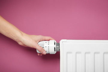 Female hand on temperature regulator of heating battery on pink background, closeup