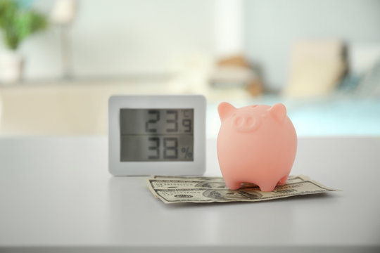 Savings Concept. Piggy Bank With Money And Electronic Thermometer On Table