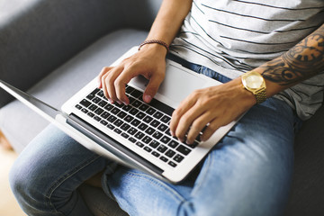 Teenage boy sitting on couch at home using laptop, partial view
