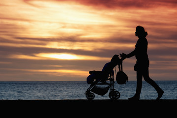 Fototapeta na wymiar Silhouette mother pulling baby stroller against beach sunset