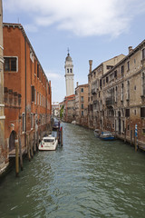 Bell tower above Venetian canal boats and vintage facades