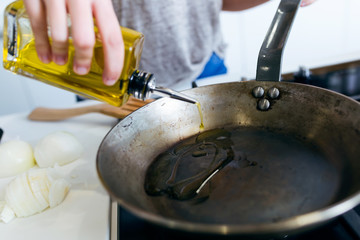 Young woman pouring oil into the pan.