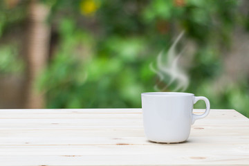 Hot coffee with steam on wooden table top on blurred garden background