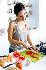 Happy young woman cutting fresh vegetables in the kitchen.