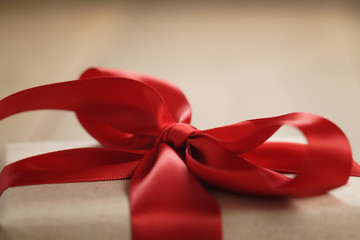 handmade gift brown paper box with red ribbon bow on wood table, close up shot