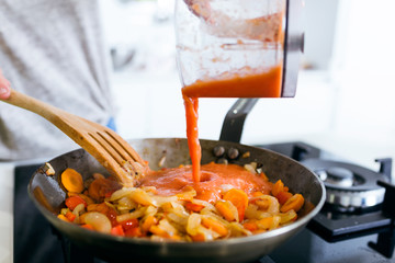 Young woman frying vegetables into the pan.