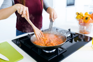 Young woman frying vegetables into the pan.