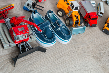 Blue boat shoes for boy near set of car toy on grey wooden background. Top view. Frame. Copy space.