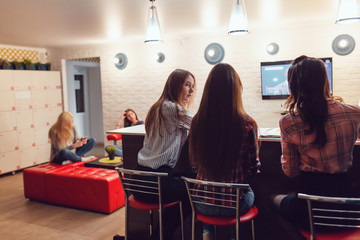 Beautiful girls sitting at the bar in Hostel, watching tv and talk.