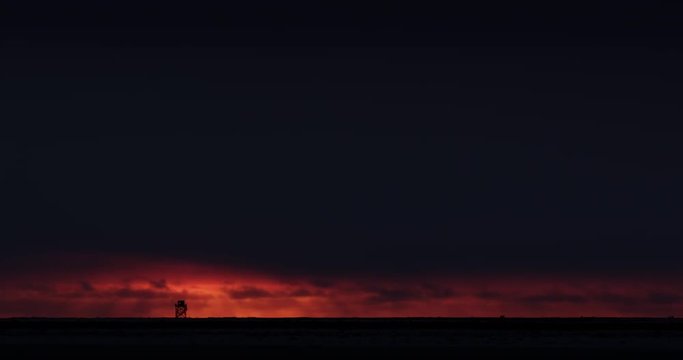 Time Lapse - clouds pass dark tower on horizon at sunset