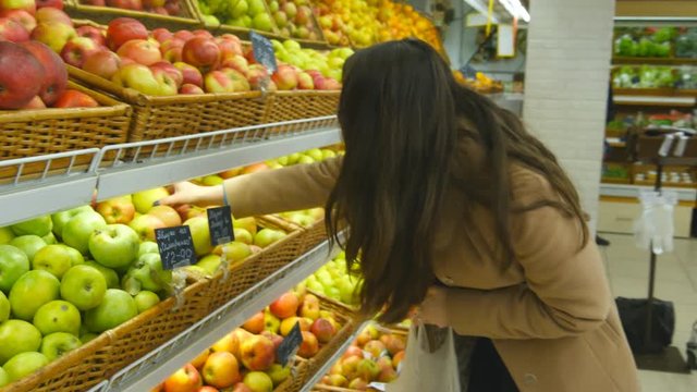 Woman selecting fresh red apples in grocery store produce department and putting it in plastic bag. Young pretty girl is choosing apples in supermarket and putting them into shop basket. Close up