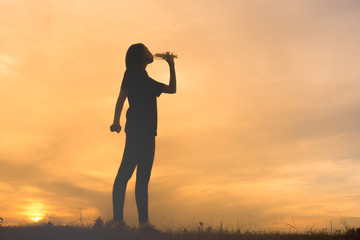 Fototapeta premium silhouette of a woman drinking water with sunset background