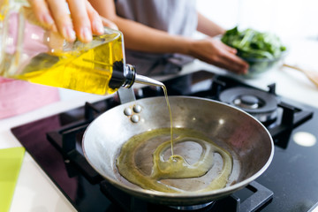 Young woman pouring oil into the pan.